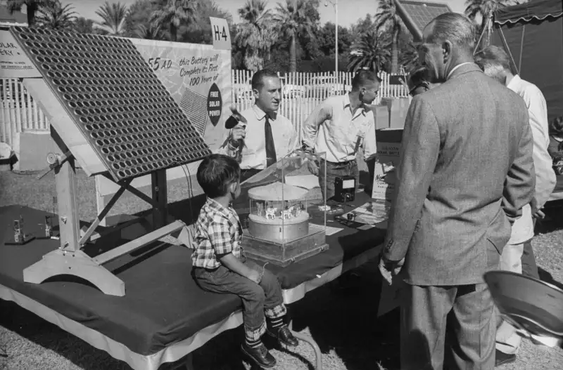 A curious young boy watches as a salesman demonstrates a solar battery.