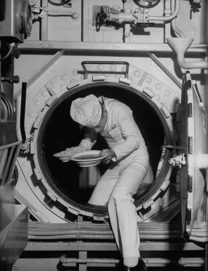 A ship's chef brings grub through a door.