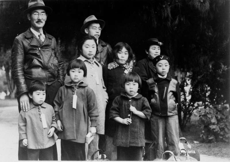 In May of 1942, members of California's Mochida family wait for the bus that will take them to an internment camp while wearing tags so they will not be separated later.