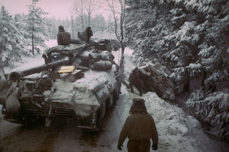 An American tank moves past another gun carriage which slid off an icy road in the Ardennes Forest, 1945.