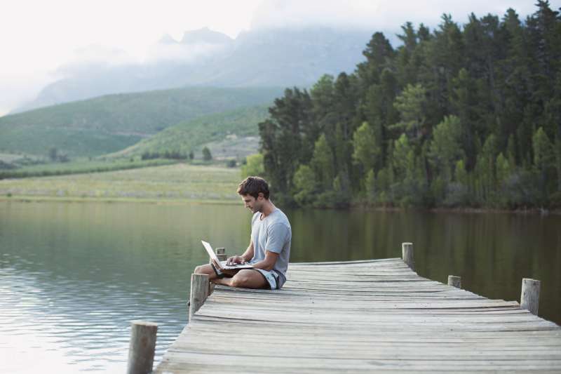 Man using laptop on dock over calm lake