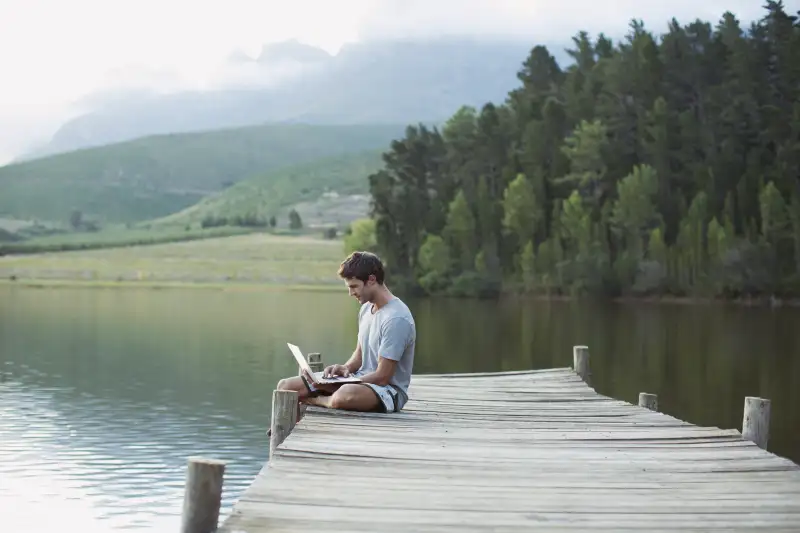 Man using laptop on dock over calm lake