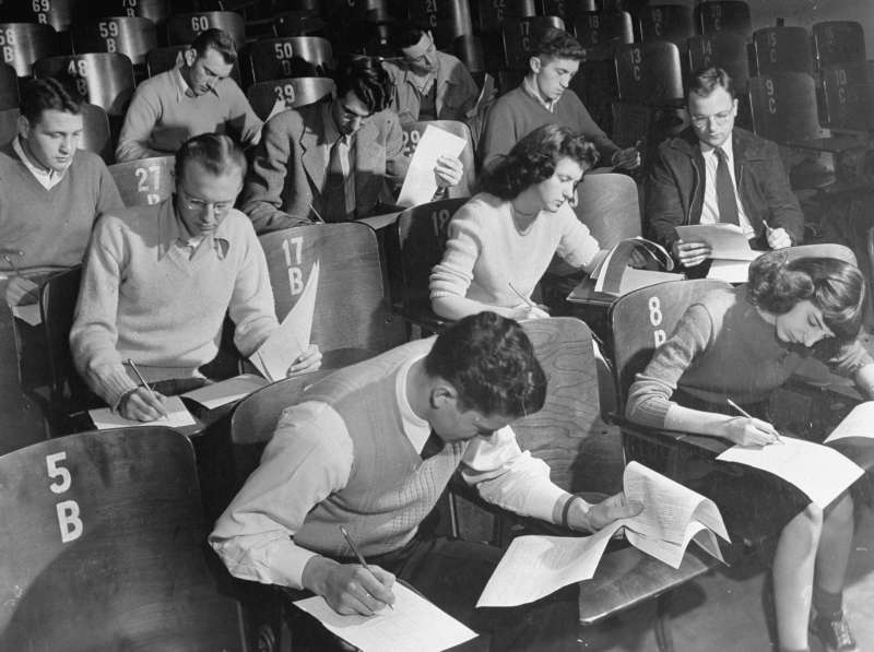 War veterans &amp; co-eds taking notes during classroom lecture at crowded University of Iowa