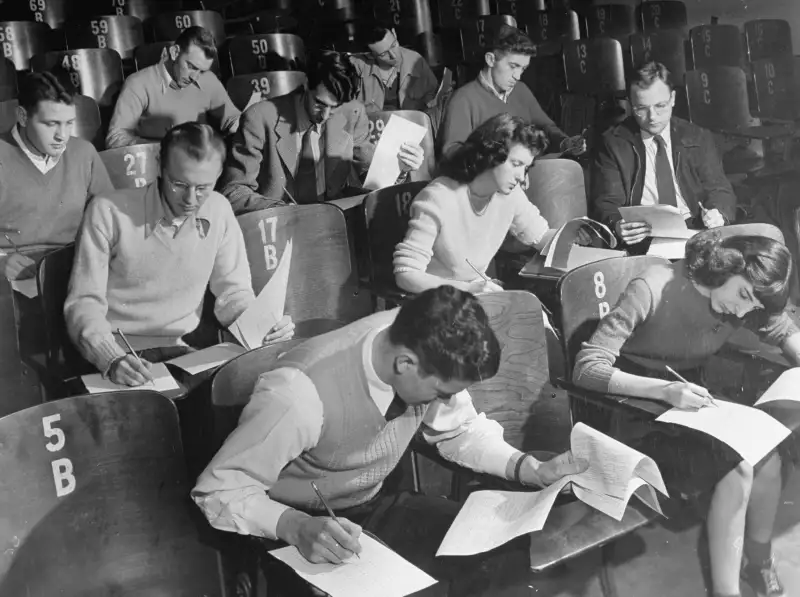 War veterans & co-eds taking notes during classroom lecture at crowded University of Iowa