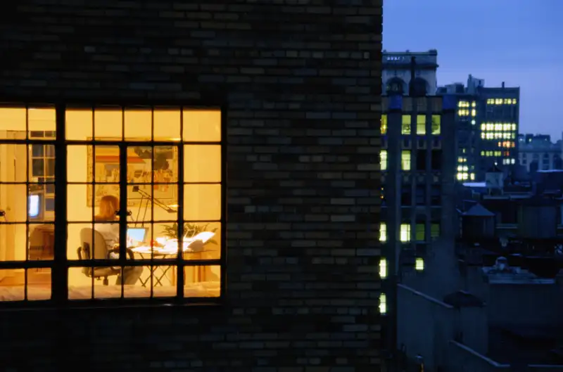 Nighttime exterior view of apartment window with woman working on laptop