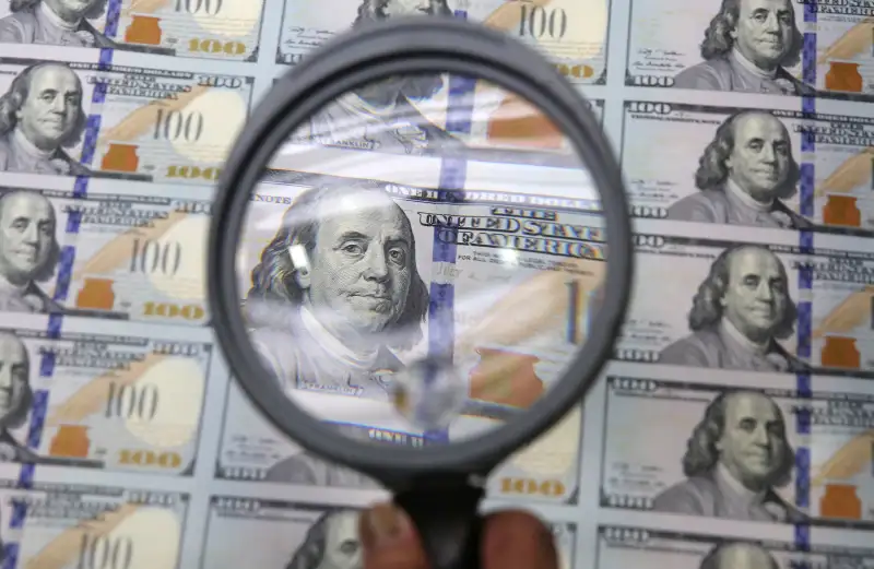 magnifying glass looking at new $100 bills