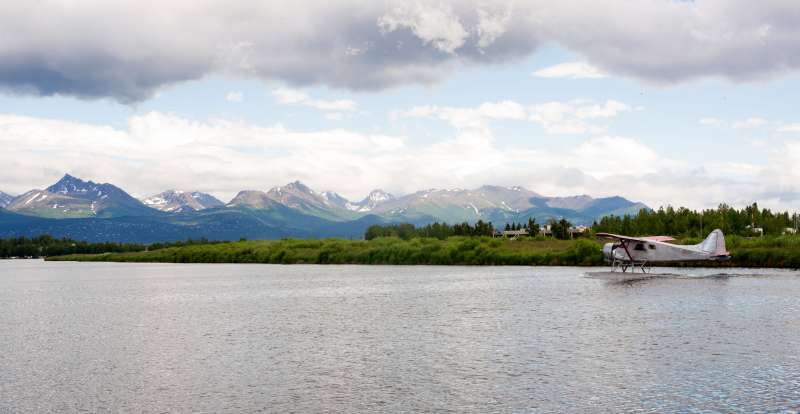 A bush plane performs take off in Alaska with Chugach Mountains in the Background.