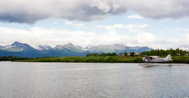 A bush plane performs take off in Alaska with Chugach Mountains in the Background.