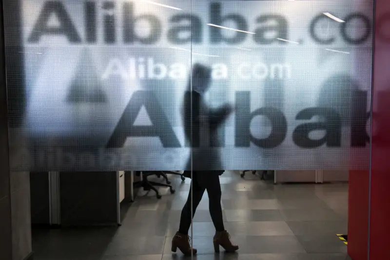 An employee is seen behind a glass wall with the logo of Alibaba at the company's headquarters on the outskirts of Hangzhou, Zhejiang