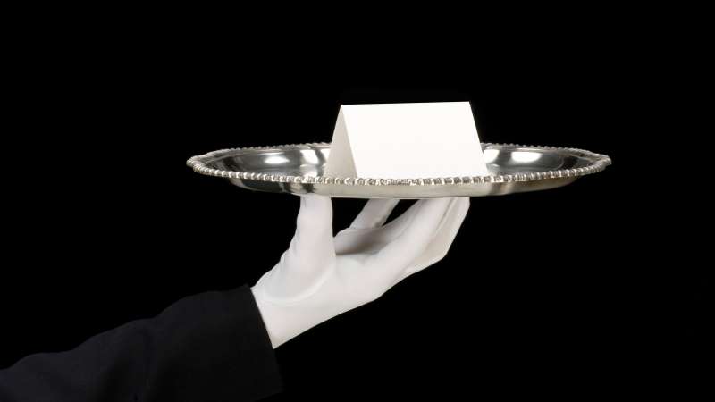 white glove waiter holding silver tray with place card