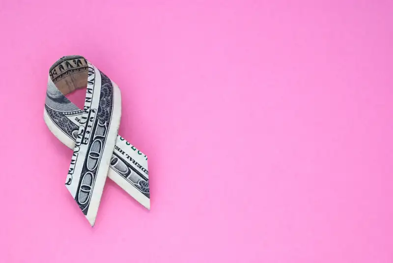 Breast cancer ribbon made out of $100 bill on pink background