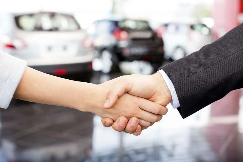 Customer and salesperson shaking hands in front of automobiles in car showroom
