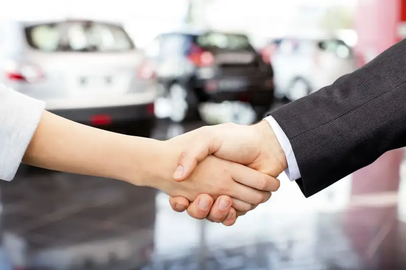 Customer and salesperson shaking hands in front of automobiles in car showroom