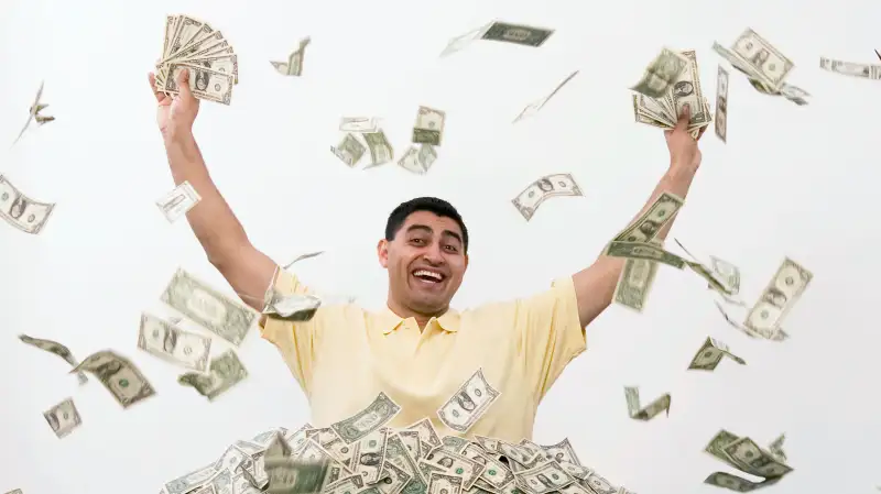 Man in pile of cash excited holding up fistfuls of money