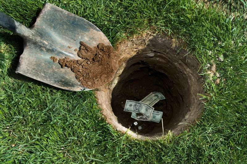 Shovel burying money in hole in backyard