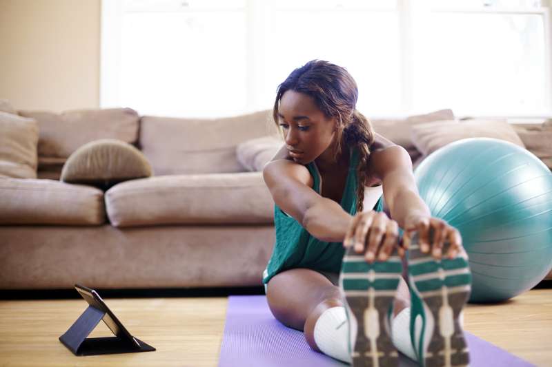 woman exercising in living room with tablet on floor next to her