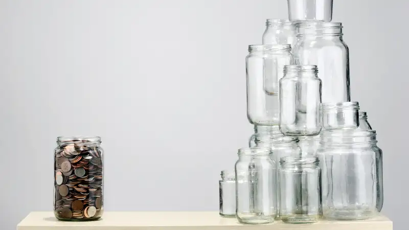 full jar of coins opposite a pile of empty jars of coins