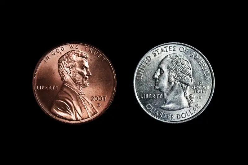 Lincoln on penny and Washington on Quarter facing one another on black background