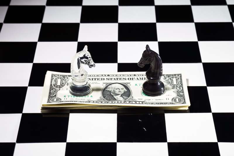 black and white chess pieces on top of stack of money on chessboard