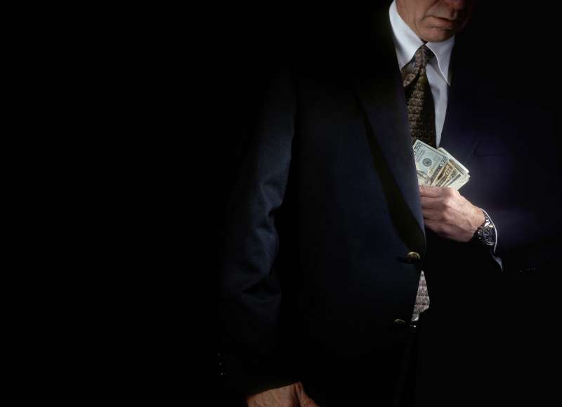 businessman putting money into his suit jacket pocket