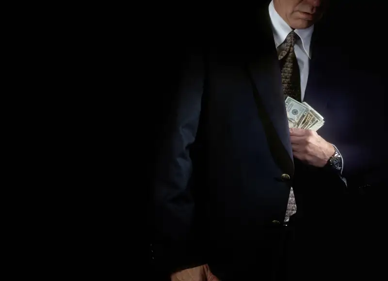 businessman putting money into his suit jacket pocket