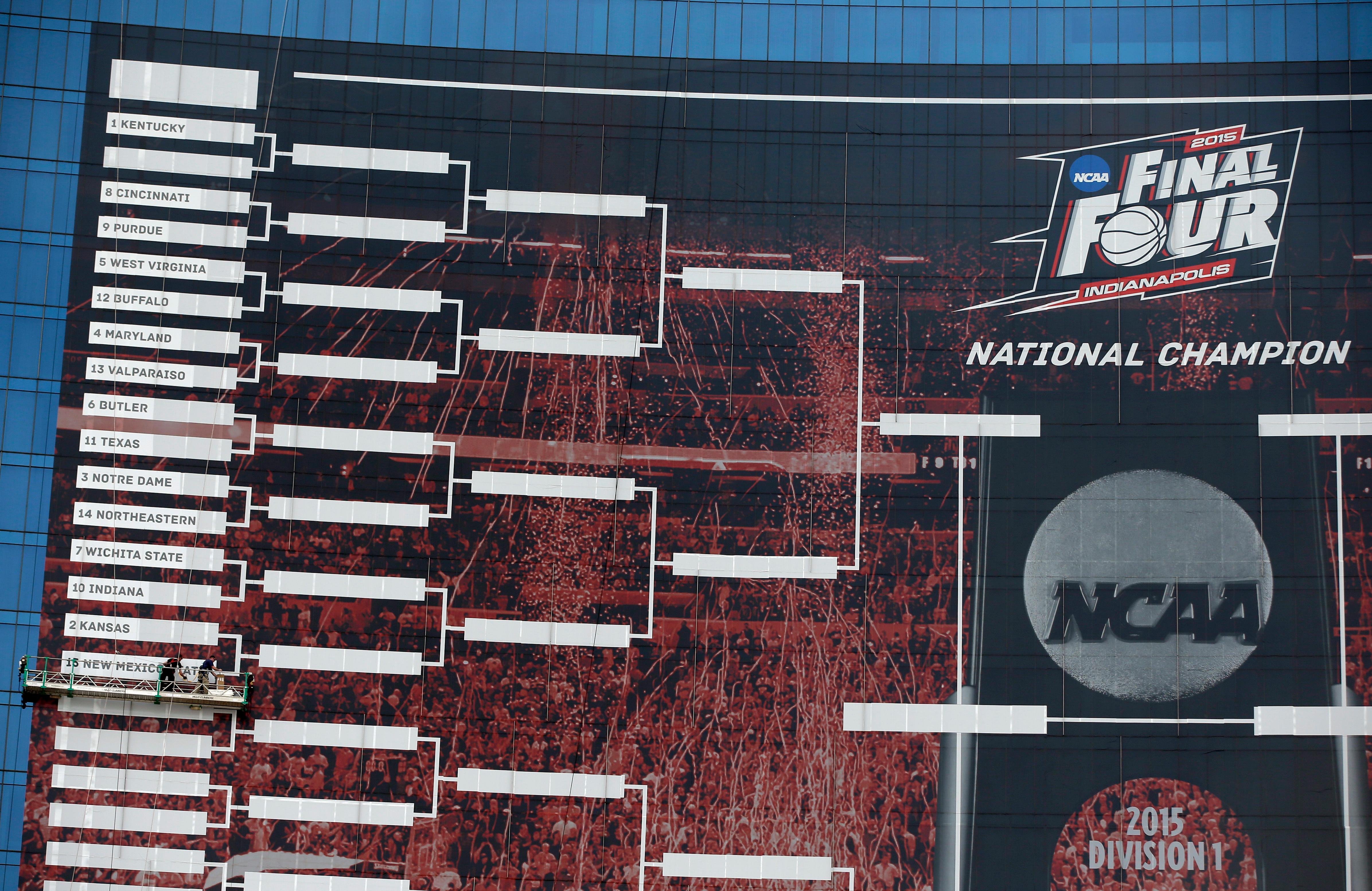 Workers add team names to a 2015 NCAA Division I Men’s Basketball Championship bracket that is displayed on the side of the JW Marriott, Monday, March 16, 2015, in Indianapolis. The championship game will be played Monday, April 6, in Indianapolis.