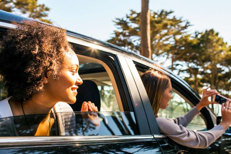 women on roadtrip, leaning out car windows
