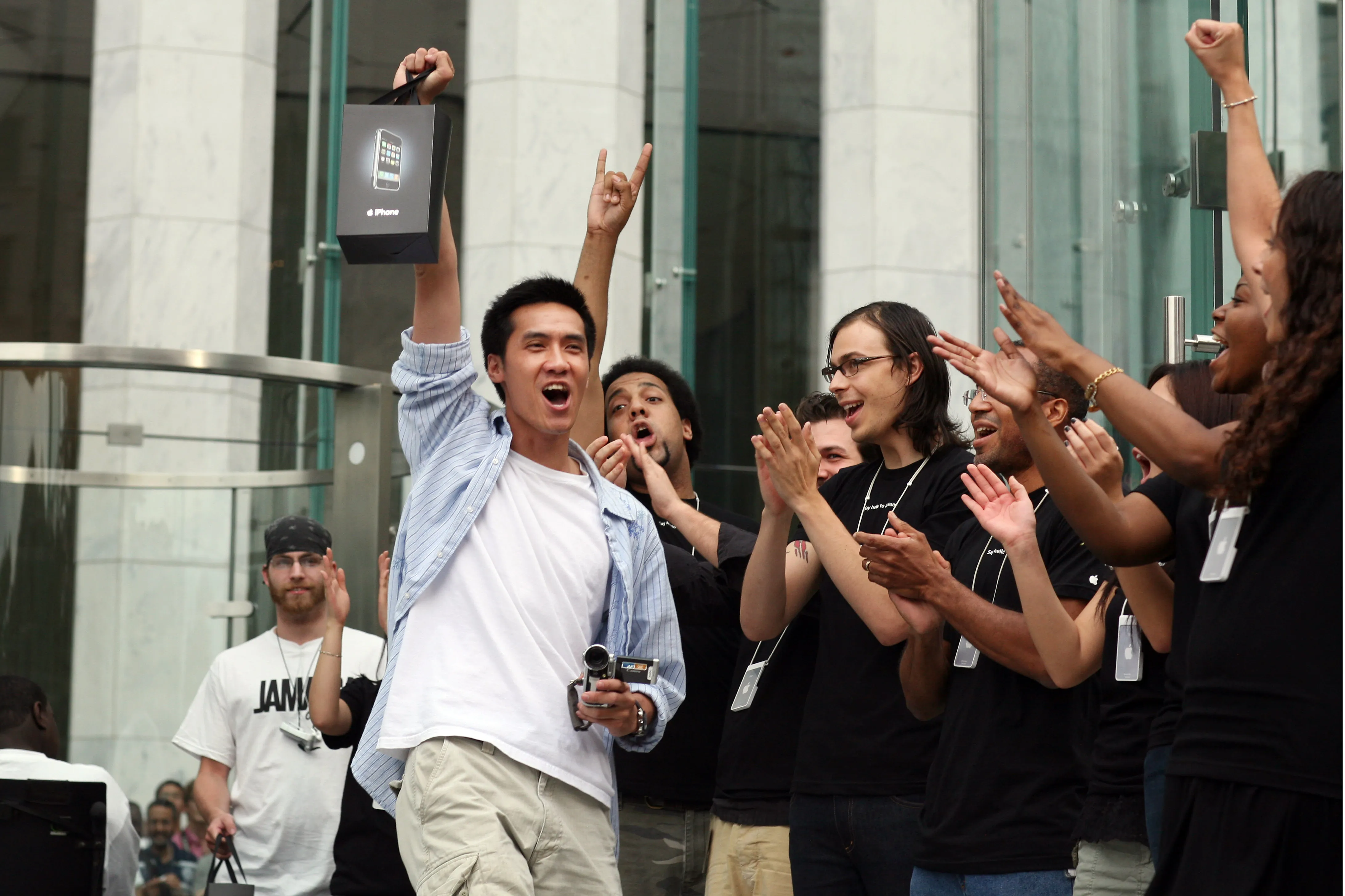 New iPhone owners exit Apple's flagship store, showing off their purchases to the media.