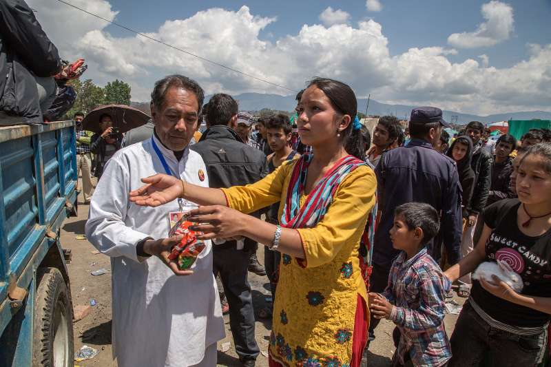 Volunteers give out packages of instant noodles to residents living in an evacuation area set up by the authorities in Tundhikel park on April 27, 2015 in Kathmandu, Nepal. A major 7.8 earthquake hit Kathmandu mid-day on Saturday, and was followed by multiple aftershocks that triggered avalanches on Mt. Everest that buried mountain climbers in their base camps. Many houses, buildings and temples in the capital were destroyed during the earthquake, leaving over 3000 dead and many more trapped under the debris as emergency rescue workers attempt to clear debris and find survivors.