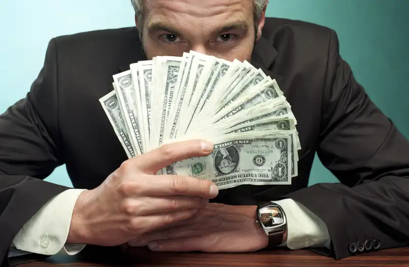 man peering over fan of cash
