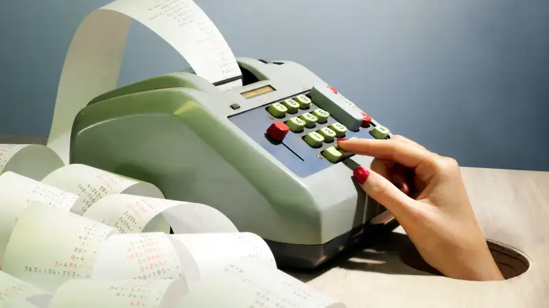 hand reaching out of hole using adding machine with rolls of paper