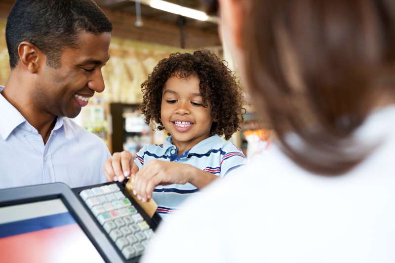father letting son swipe credit card at cash register