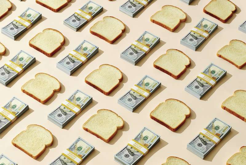 slices of bread and stacks of $100 bills on peach background