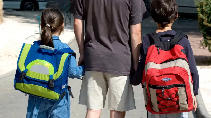 parent holding hands with two kids with backpacks