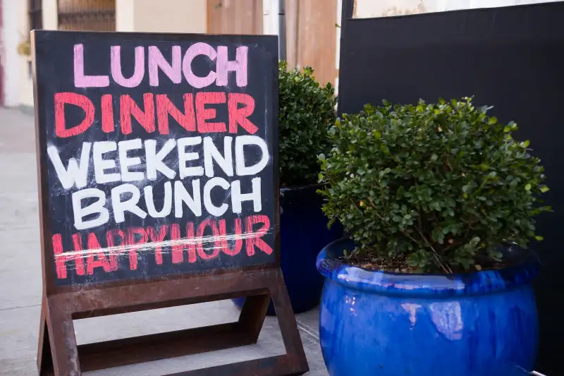 chalkboard sign on sidewalk announcing lunch, dinner, weekend, brunch, happy hour with the happy hour crossed out