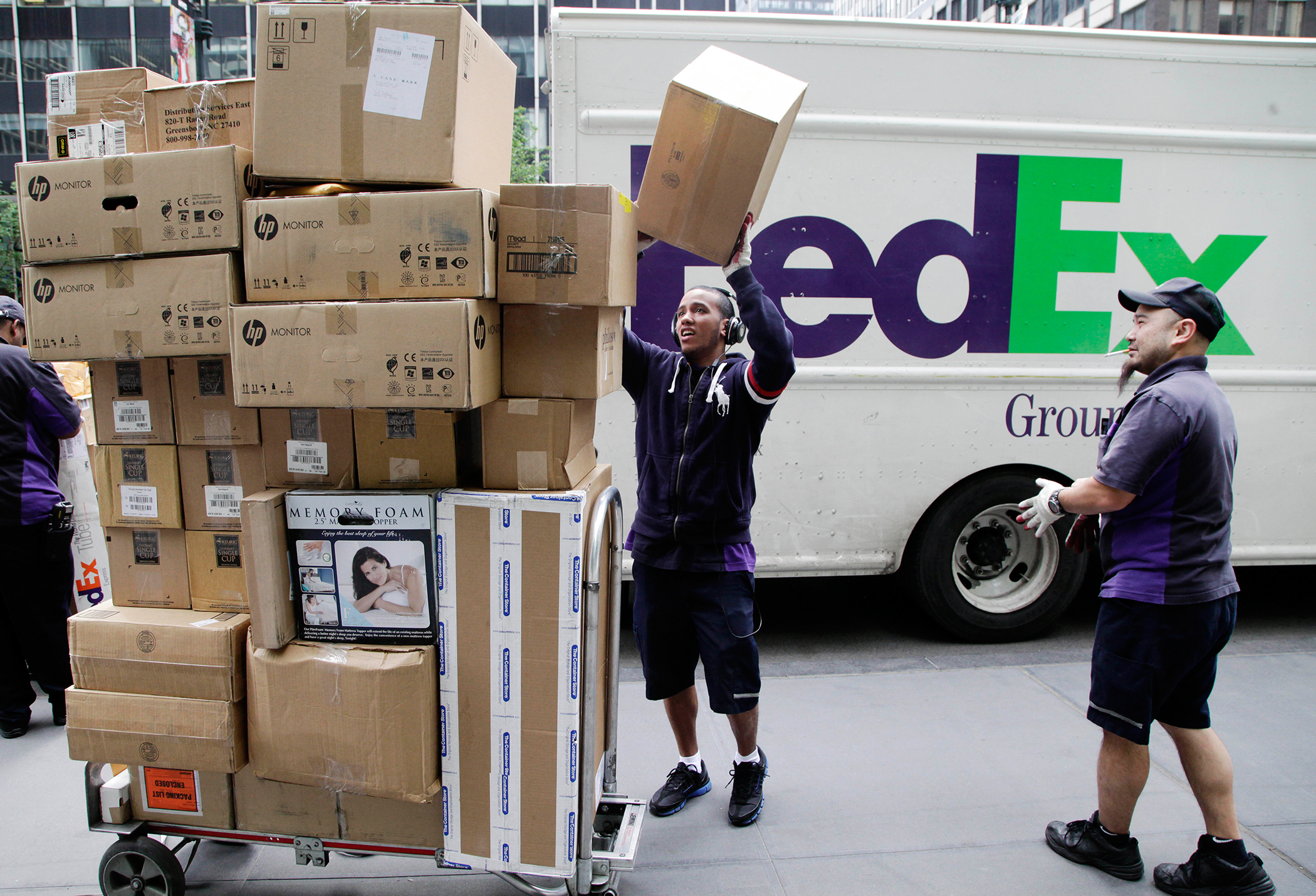FedEx Ground deliverymen throwing a box onto a stack