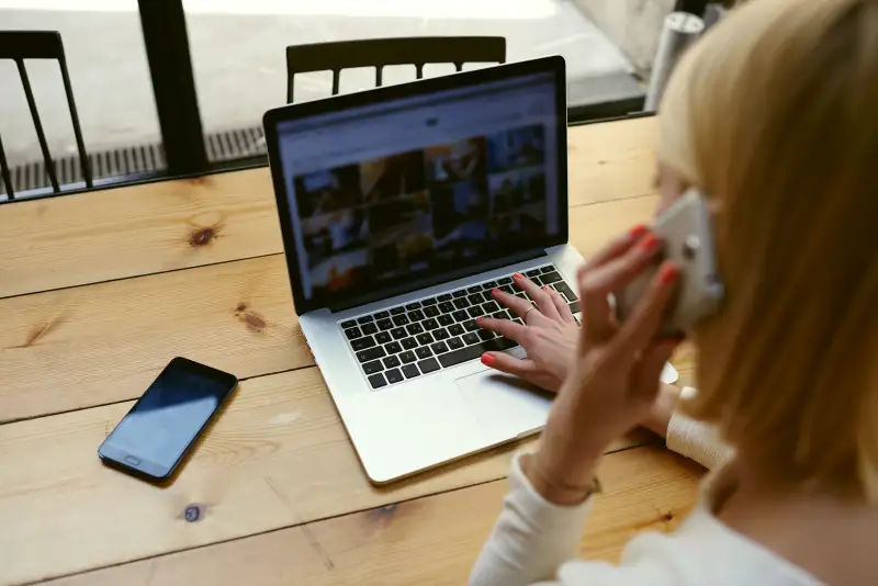 woman working on laptop and talking on cell phone in coffee shop