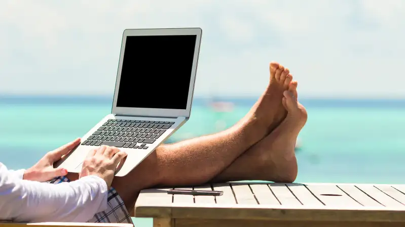 man typing on laptop with ocean view in background