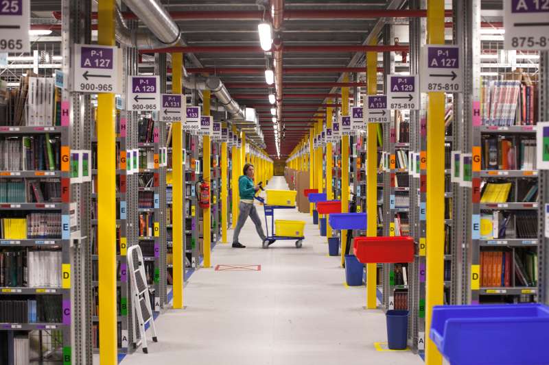 An employee pushes a cart past bays of merchandise as she processes customer orders at the Amazon.com Inc. fulfillment center in Poznan, Poland, on Friday, June 12, 2014.