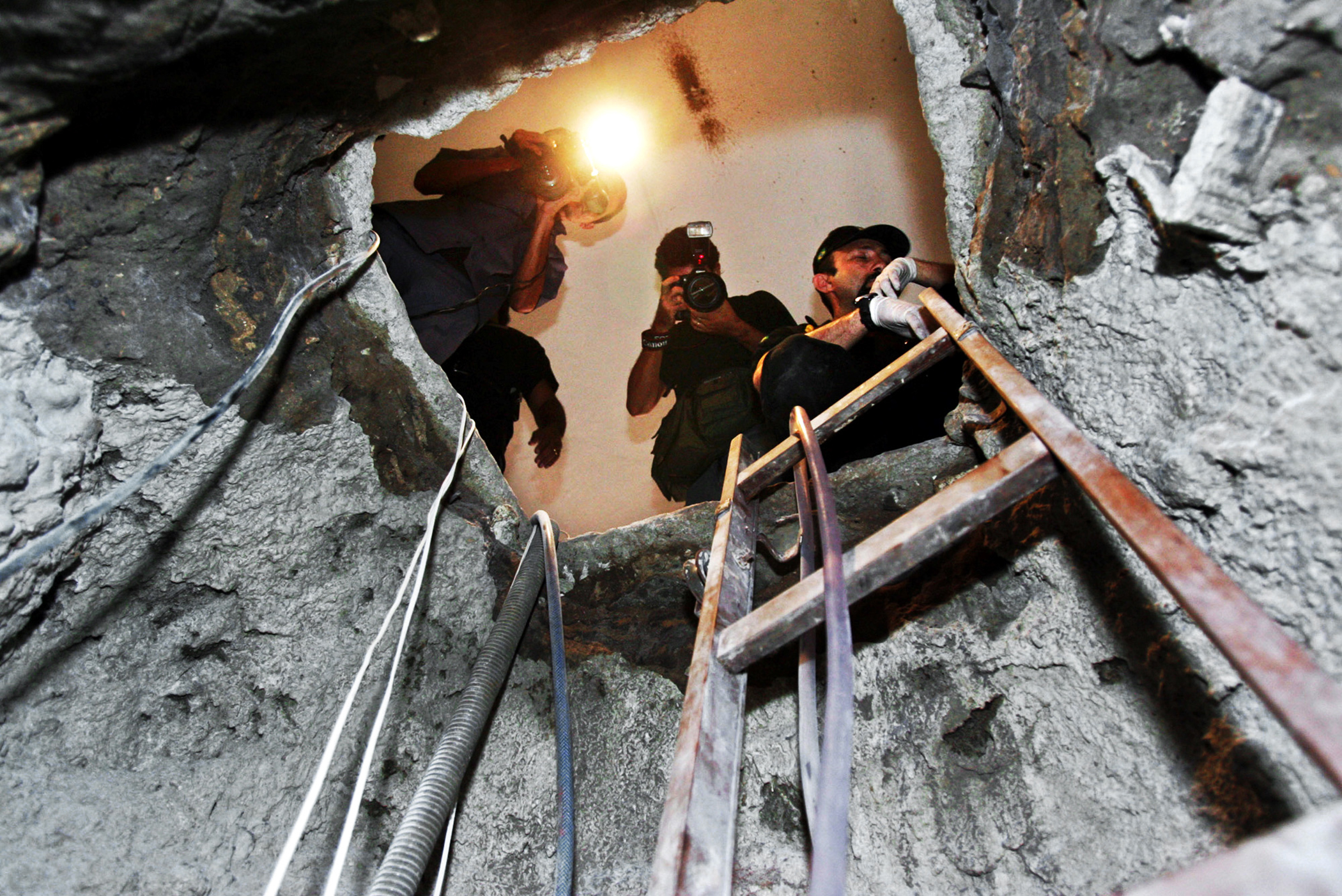 Police and reporters look at the tunnel where highly sophisticated thieves spent three months digging under a busy city avenue to break into a Brazilian Central Bank in Fortaleza, Brazil, Monday, Aug. 8, 2005. The crime, which netted 150 million reals (US$65 million, 53 million), was the biggest robbery ever in Brazil.