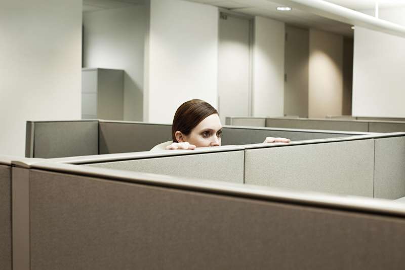 Woman hiding behind cubicle in office