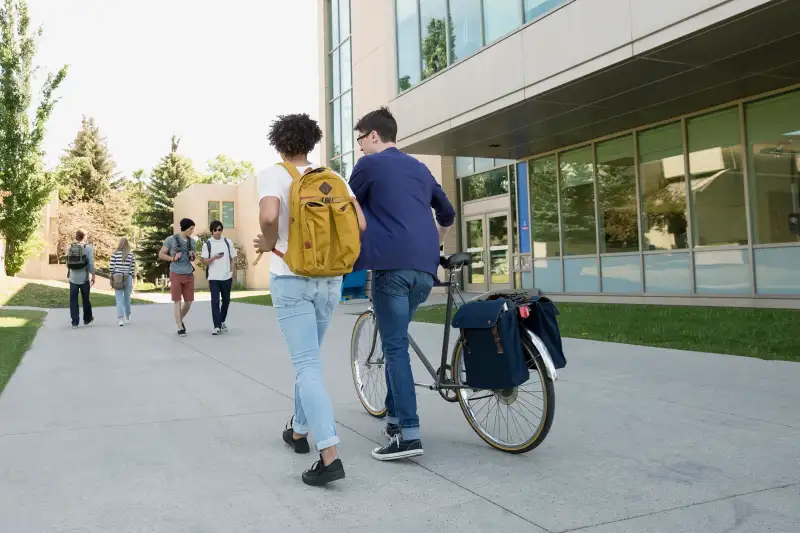 College students with bicycle walking on campus sidewalk