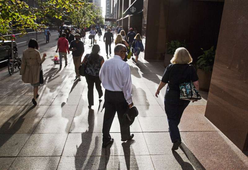 Commuters walk down a sidewalk lit by the rising sun in New York, September 29, 2015.