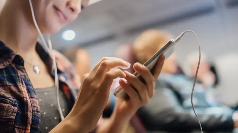 woman using smartphone and headphones on airplane