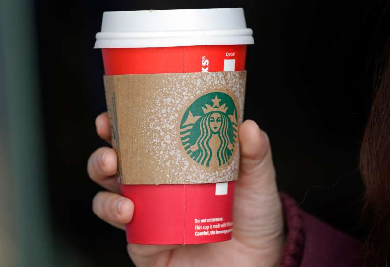 A customer carries a coffee drink in a red paper cup, with a cardboard cover attached, outside a Starbucks coffee shop in the Pike Place Market, November 10, 2015, in Seattle.