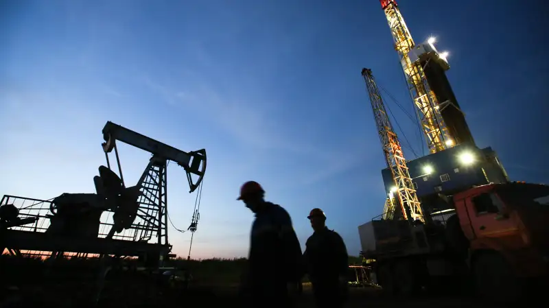 Oil workers pass a pumping unit, also known as a  nodding donkey  or pumping jack, left, at a drilling site operated by Tatneft OAO near Almetyevsk, Russia, on Friday, July 31, 2015.