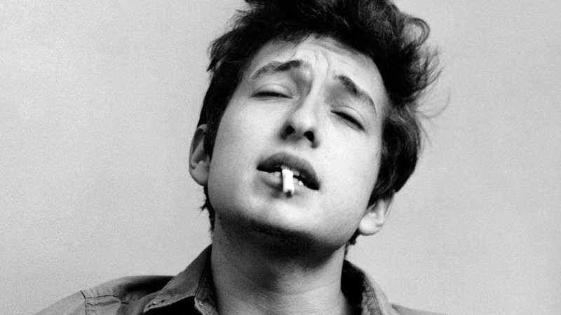 Bob Dylan plays acoustic guitar and smokes a cigarette in this headshot from September 1961 in New York City, New York.