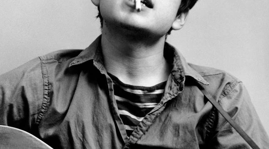 Bob Dylan plays acoustic guitar and smokes a cigarette in this headshot from September 1961 in New York City, New York.