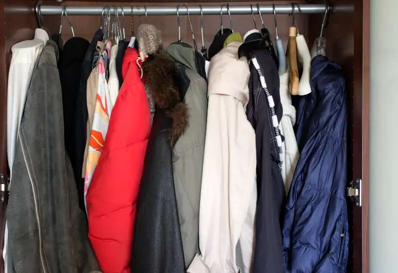 Various clothes, leather jacket with fur collar hanging in the wardrobe