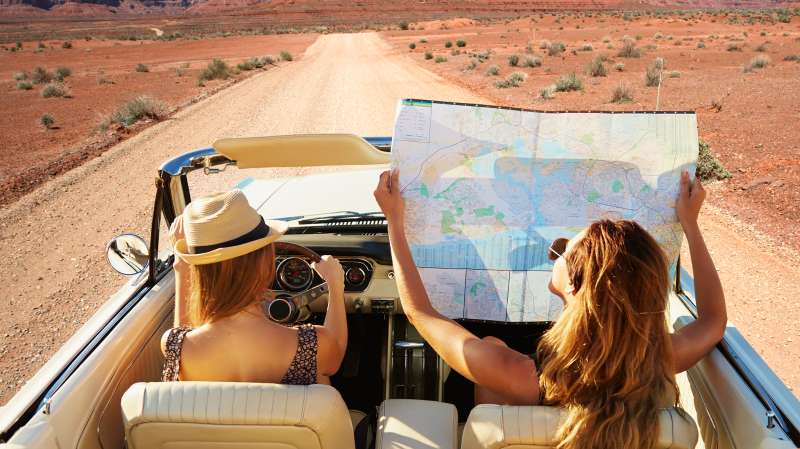 girls in convertible with roadmap in desert
